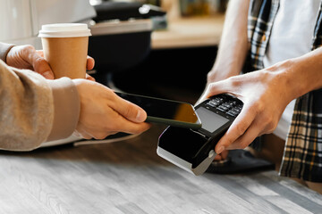 A man pays with a smartphone in a coffee shop for a cup of coffee. Purchase concept