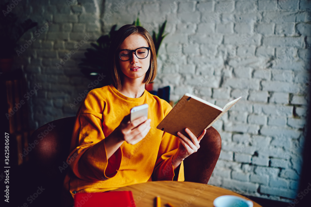 Aufkleber young businesswoman holding notepad for notes while reading incoming notification on smartphone devi