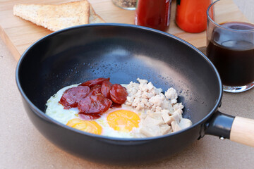 pan fried egg with toppings, Chinese sausage and pork sausage in the black pan.