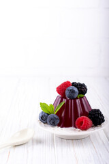 Sweet dessert jelly pudding with berries raspberries blackberries blueberries on white plate