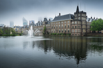 Fototapeta na wymiar Binnenhof palace, place of Parliament in The Hague, Netherlands mirrored in the Hofvijver on a foggy day. Left the museum Mauritshuis
