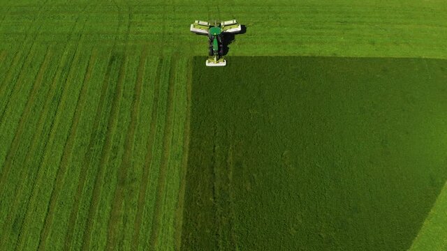 Aerial view over green tractod mowing vivid saturated green field of wheat