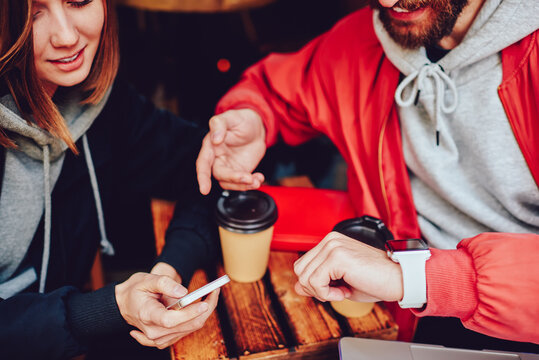 Cropped view of two millennial hipster friends dressed in casual wear checking time on modern wristwatch and digital smartphone resting together and using free 4G internet connection - Powered by Adobe