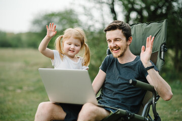 Father work on Internet with kid outdoors. Quarantine, closed nursery school during coronavirus outbreak. Communication with family online on laptop on picnic in nature. Homeschooling, freelance job.