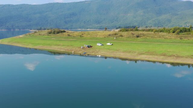 Cars parked on Rama Lake in Bosnia and Herzegovina shore near a small campsite, Aerial dolly in shot