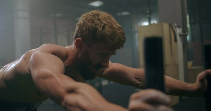 Close-up: a tenacious purposeful male athlete pushes a heavy sled in the gym. exercise with a heavy weight for endurance. Sports spirit of victory