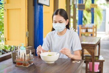 A young woman is eating Thai Street food , wearing face mask, New normal eating concept