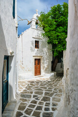 Fototapeta na wymiar Picturesque scenic narrow Greek streets with traditional whitewashed houses with blue doors windows of Mykonos town and orthodox church in famous tourist attraction Mykonos island, Greece