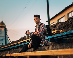 A young man sitting on a bench drinking a coffe outdoors