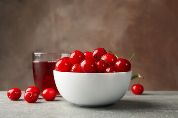 Bowl with red cherry and glass of juice on gray table, space for text