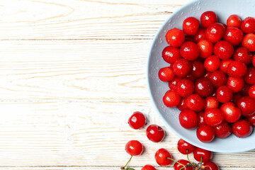 Plate with red cherry on white wooden background, top view