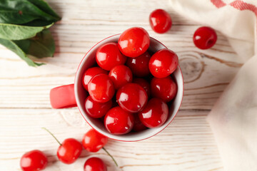 Cup with cherry and towel on white wooden background, top view