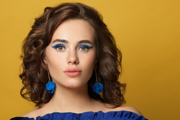 Young brunette model woman with curly bob haistyle and blue earrings on vivid yellow background
