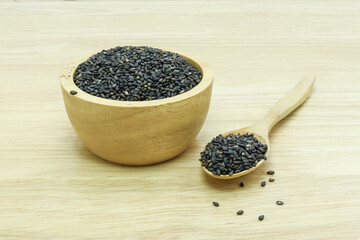 Black sesame seeds in wooden spoon pile on wood table