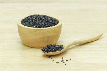 Black sesame seeds in wooden spoon pile on wood table