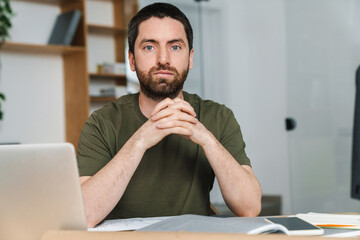Fototapeta premium Photo of man looking at camera while working with laptop and drawings