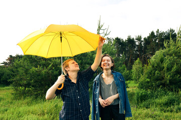 Two happy young lesbian girls under yellow umbrella in forest outdoors on a nice summer day, with copyspace