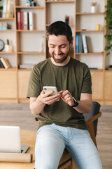 Photo of man smiling and using cellphone while sitting on table