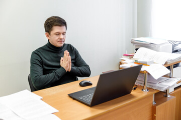 Naklejka premium Relaxed corporate man sitting with closed eyes contemplating at work desk with laptop in office. Guy relaxing, relieves stress, gets positive thinking with yoga exercise. Stress free workplace concept