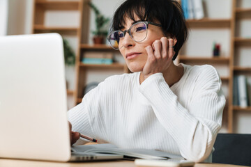 Photo of pleased woman working with laptop while sitting at table