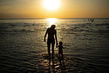 Mother and the son walking in the sunset in the sea
