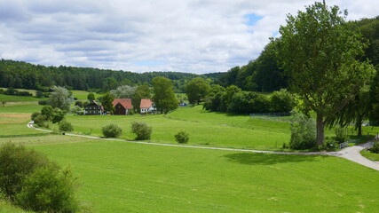 Wanderweg in einer herrlichen Heckengäulandschaft mit Wiese, Bäumen, Hecken, Wanderweg und Bauernhof