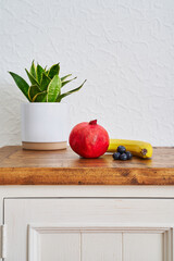 Granatapfel, Beeren und Banane mit einer Pflanze auf einem Sideboard. Stylish Interieur.