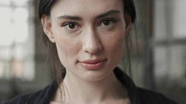 A close-up view of a young calm businesswoman is opening her eyes and looking to the camera standing in the office