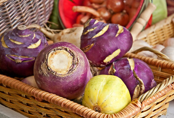 This still life of root vegetables is purple turnips in a wicker basket with other vegetables surrounding them.  They are whole, uncut veggies.