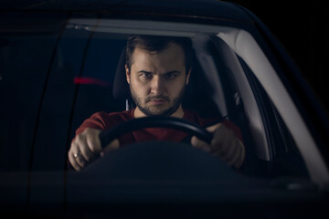 Portrait of Unshaven confident serious male driver sits at steering wheel of car at night focused looking ahead. Loneliness Concept. man spending time alone at car worried concerned about problems