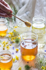 A honey jar with a spoon for honey in hand with flowers in background, selektive focus, backlight