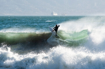 Surfer on the crest of the wave, seen from Re&ntilde;aca beach, central coast of Chile. In the background, a ship arriving at the port of Valparaiso