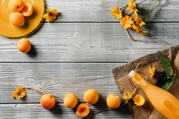 Food frame with apricots, a bottle of juice and yellow flowers on a wooden background with copy space