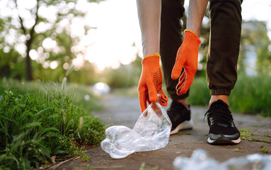 Empty plastic bottles in the park. Garbage collection in the park. Men hand  wearing protective gloves collects bottle plastic. Save nature.