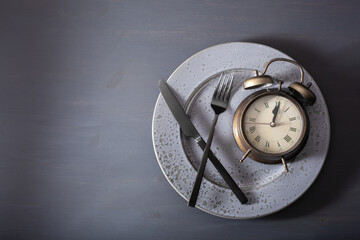 concept of intermittent fasting, ketogenic diet, weight loss. fork and knife, alarmclock on plate