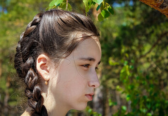Portrait of a teenage girl with a serious face in profile against the background of nature.