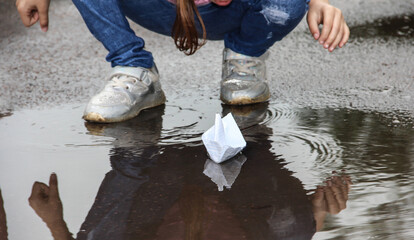 A paper boat in a muddy puddle and children's feet.