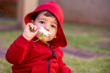 Baby in red hooded winter sweater smelling a flower.