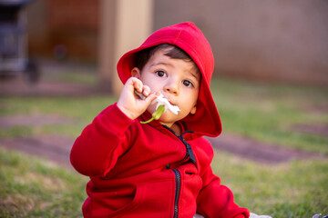 Baby in red hooded winter sweater smelling a flower.