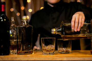 Waitress man standing pours whiskey into a glass 