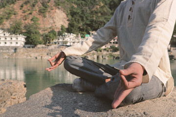 A young Indian guy sits in a lotus position on the banks of the Ganges in Rishikesh. The practice of meditation in nature. Yoga in India.