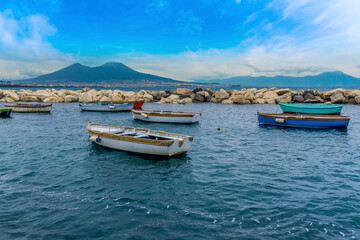 Fototapeta na wymiar Fishing boats moored in front of the marina breakwater in Naples, Italy with Mount Vesuvius in the distance