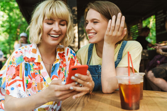 Image of two women using cellphones and laughing while drinking soda