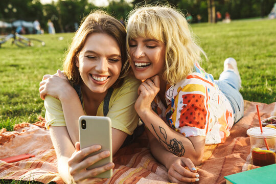 Image of joyful two women taking selfie on cellphone while have picnic