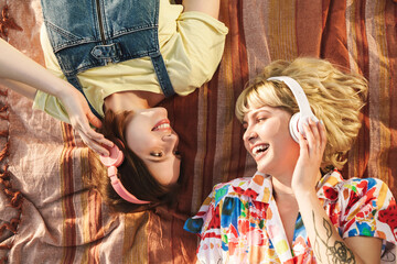 Obraz premium Image of two women using wireless headphones while lying on blanket