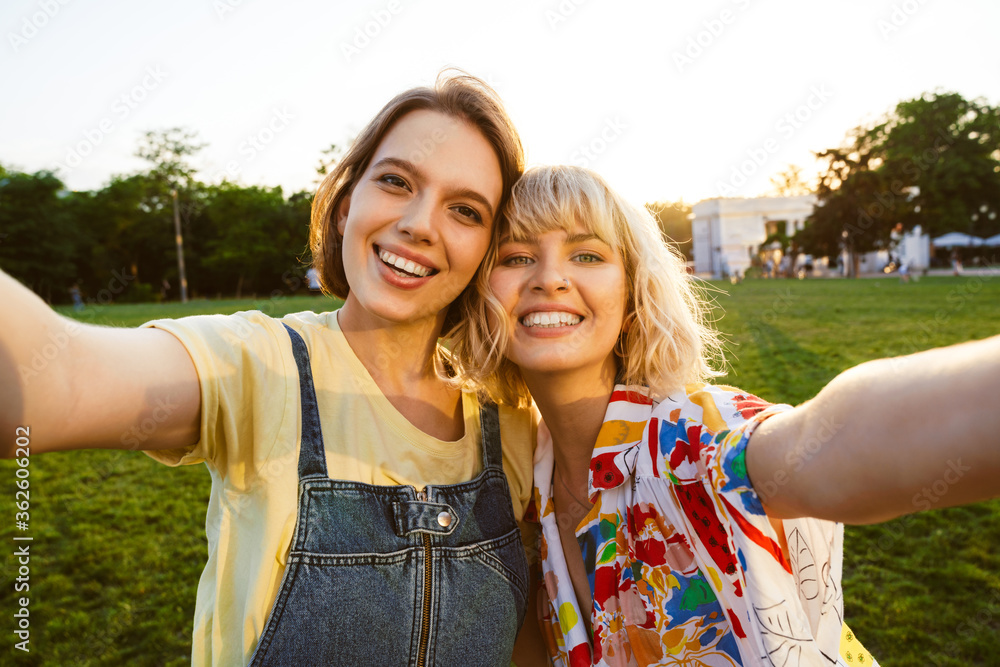 Wall mural Image of cheerful attractive two women taking selfie photo and hugging