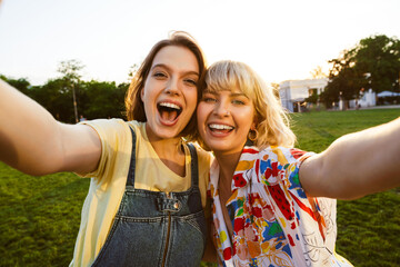 Image of cheerful attractive two women taking selfie photo and hugging