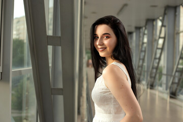 Portrait of a beautiful brunette in a light dress on the street in a pedestrian crossing on a summer day