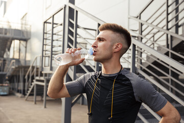 Image of unshaven caucasian sportsman drinking water while working out