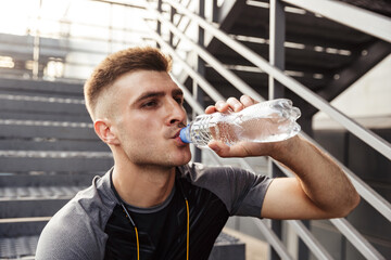 Fototapeta na wymiar Image of unshaven sportsman drinking water while sitting on stair